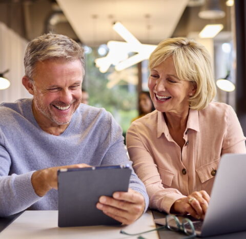 Mature Male And Female Business Colleagues Meeting Using Laptop And Digital Tablet In Modern Office