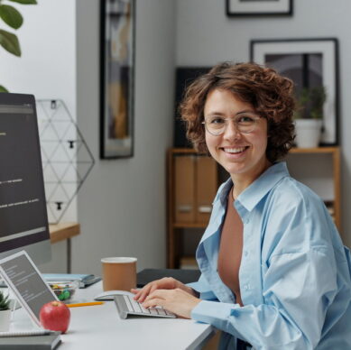 Portrait of female developer smiling at camera while working on computer with codes at office