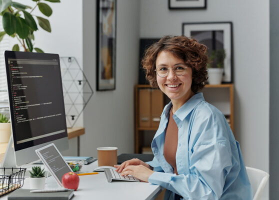 Portrait of female developer smiling at camera while working on computer with codes at office